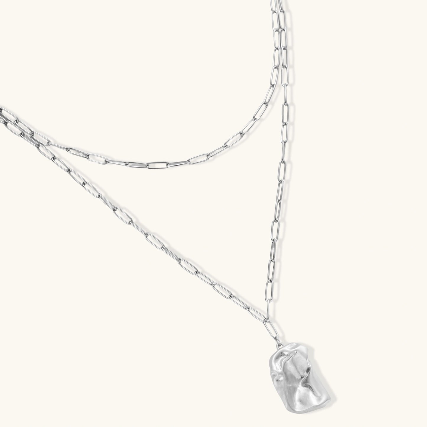 Silver layered necklace with organic flowing pendant in eco-zinc alloy on neutral background, showing adjustable chain design.